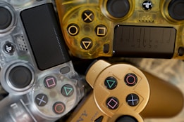 A collection of three gaming controllers with distinct designs and colors. The designs feature translucent materials and unique button symbols. The controllers are intricately arranged, showcasing various textures and materials.