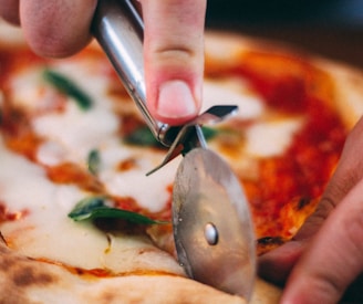 person holding stainless steel knife slicing pizza