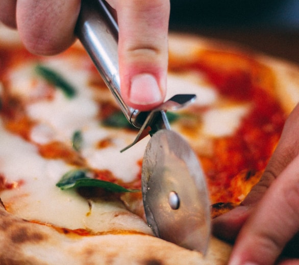 person holding stainless steel knife slicing pizza