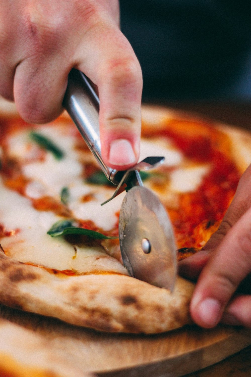 person holding stainless steel knife slicing pizza