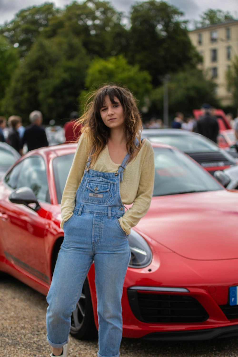 woman in brown cardigan standing beside red car during daytime