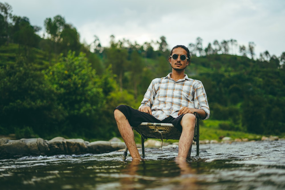 man in white and blue plaid dress shirt sitting on black armchair on river side during