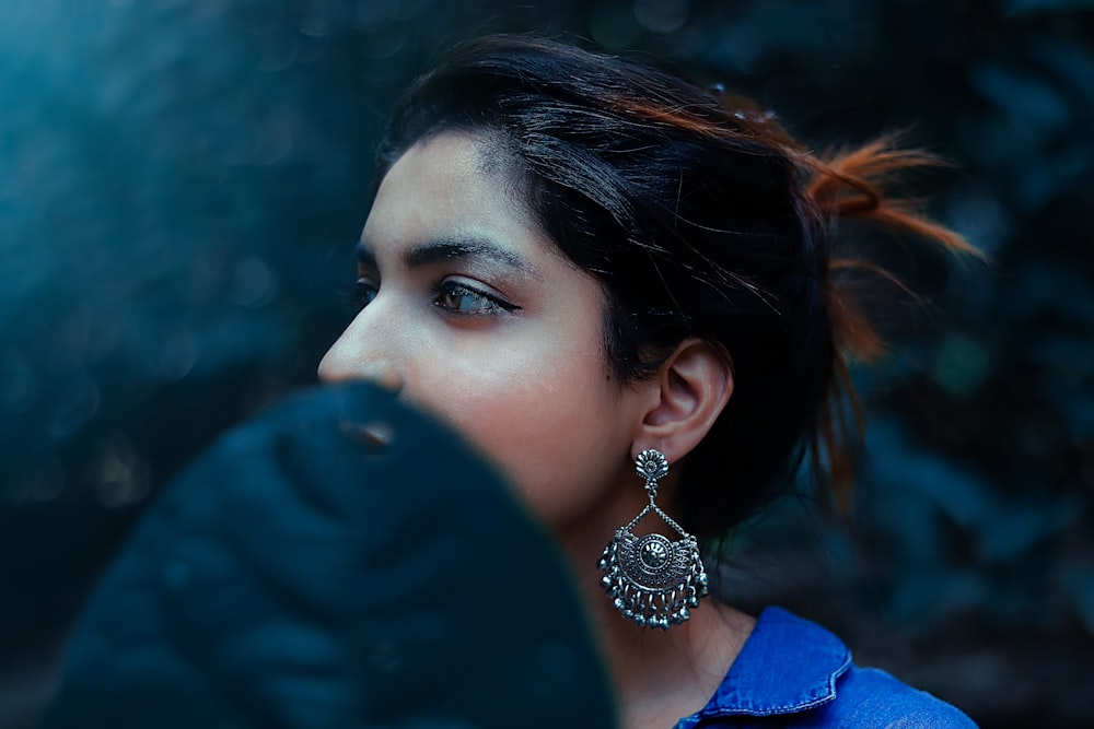 woman in blue shirt wearing silver and diamond drop earrings