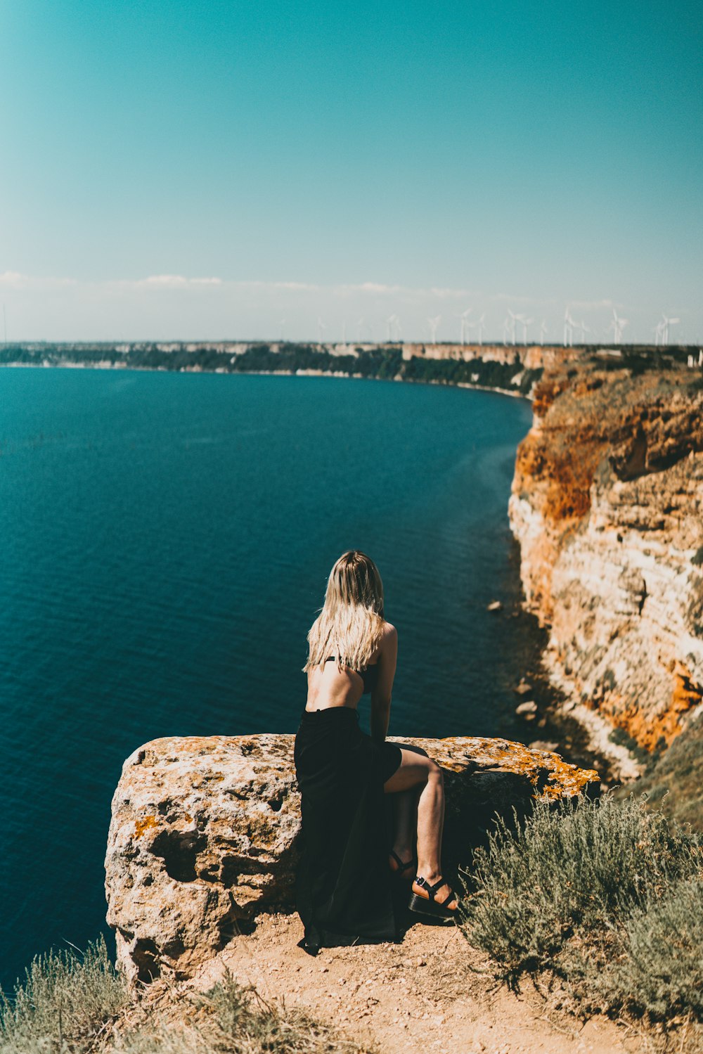 donna in vestito nero che si siede sulla formazione rocciosa guardando il mare durante il giorno