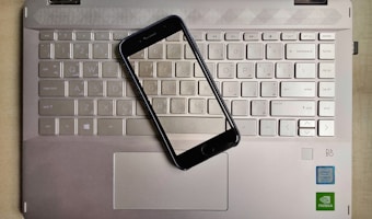 A smartphone is placed on top of a laptop keyboard. The keyboard is part of a metallic laptop, and the smartphone is positioned diagonally across the keys. The laptop features visible logos near the bottom right corner, including Intel and NVIDIA stickers, indicating the hardware specifications.