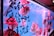 An aquarium tank filled with vibrant goldfish swimming against a bright blue backdrop. Black Chinese characters are painted or printed on the outside of the tank, adding a cultural and artistic element. The lighting casts a pinkish hue, creating a warm and inviting atmosphere.