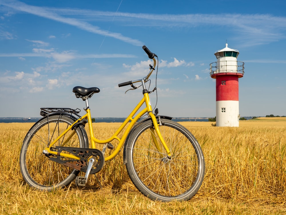 Bicicleta amarilla cerca del faro rojo y blanco bajo el cielo azul durante el día