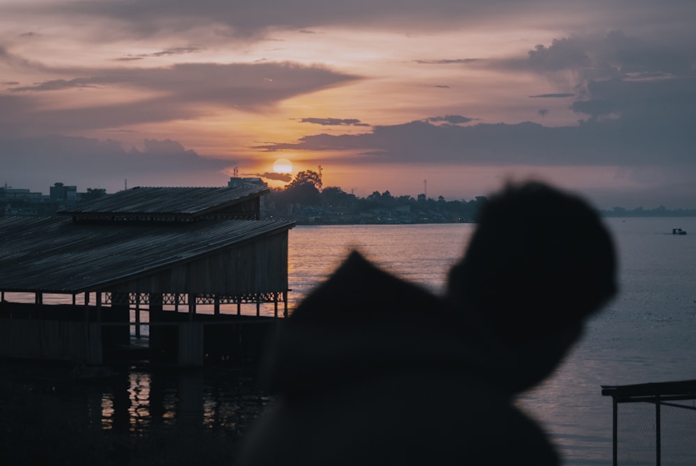 silhouette of person sitting on dock during sunset