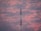 A telecommunications tower stands prominently against a backdrop of a vibrant, cloudy sky. The clouds are painted in hues of pink and purple, suggesting a sunset or sunrise.