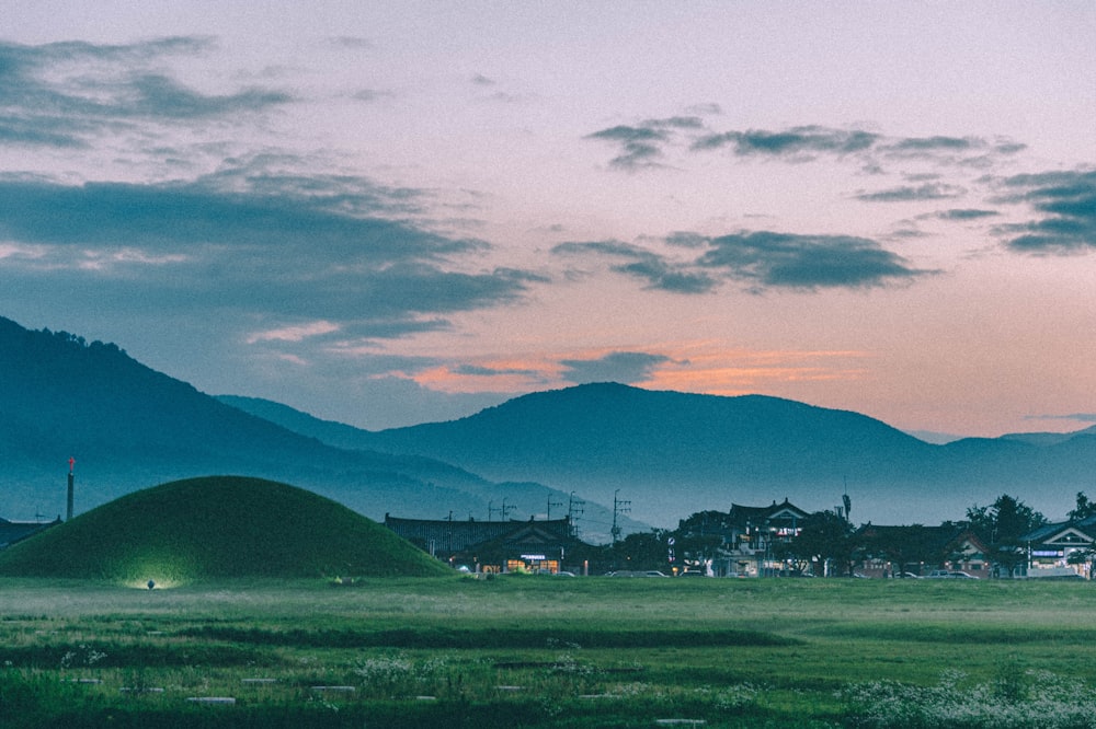 green grass field near mountain under cloudy sky during daytime