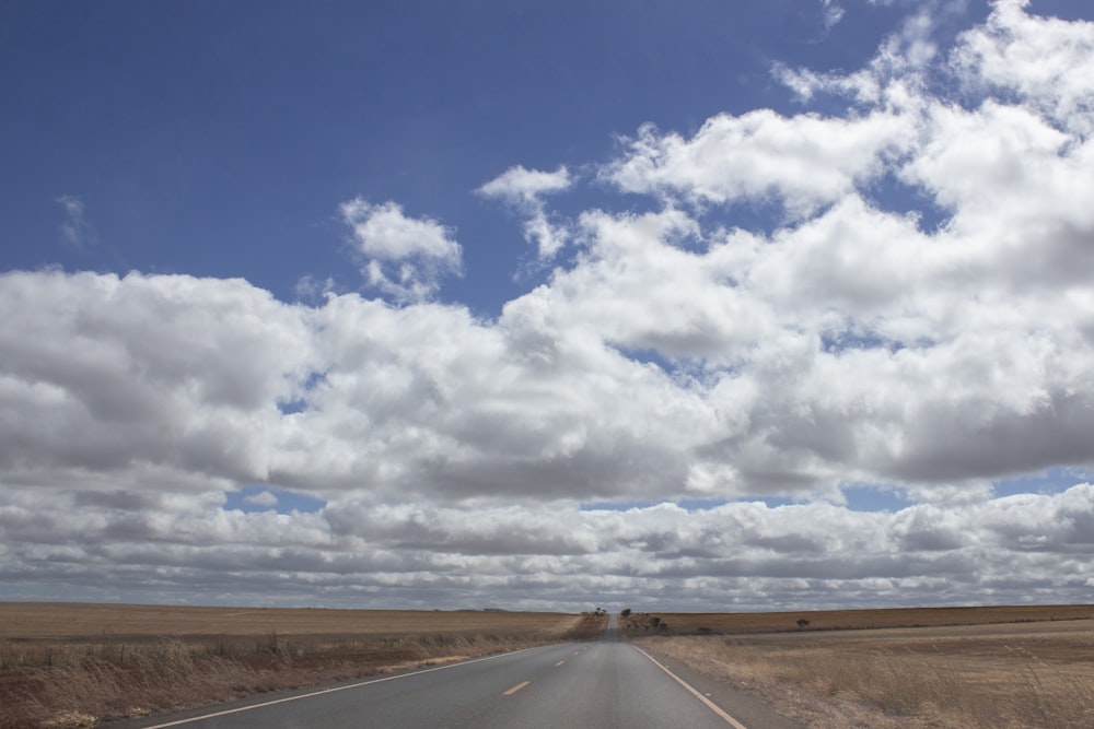 Route goudronnée grise sous un ciel nuageux bleu et blanc pendant la journée