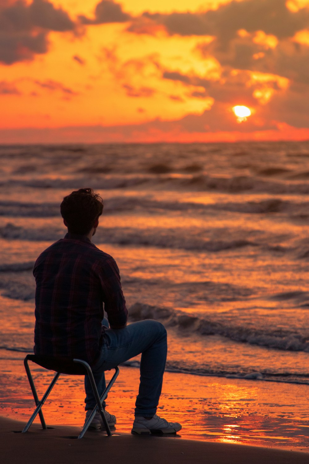 Homme en jean bleu assis sur une chaise au coucher du soleil