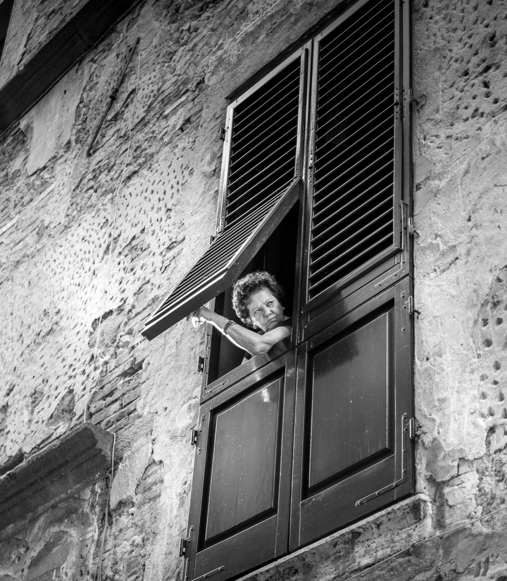 grayscale photo of woman in window