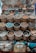 Handcrafted, colorful bowls and plates with intricate designs are displayed on a surface, along with bamboo baskets filled with a variety of spices, nuts, and other natural materials. Cushions with artistic designs are placed at the bottom of the display.