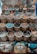 Handcrafted, colorful bowls and plates with intricate designs are displayed on a surface, along with bamboo baskets filled with a variety of spices, nuts, and other natural materials. Cushions with artistic designs are placed at the bottom of the display.