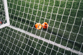 A close-up of a football on a black and white pitch with a red corner flag waving gently.