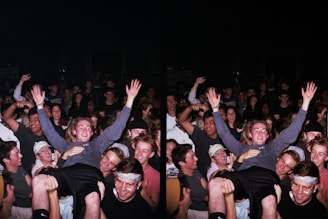 A large group of people gathered in a celebratory atmosphere, many smiling and raising their hands. The central figure is hoisted above the crowd, suggesting a lively, energetic event.