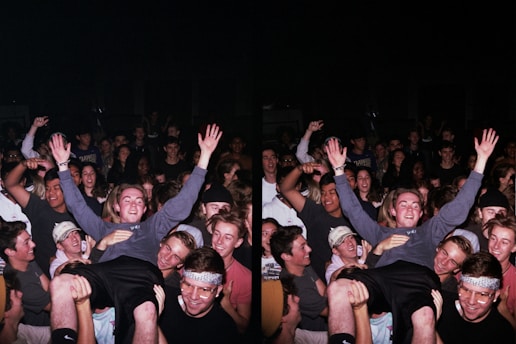 A large group of people gathered in a celebratory atmosphere, many smiling and raising their hands. The central figure is hoisted above the crowd, suggesting a lively, energetic event.