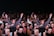 A large group of people gathered in a celebratory atmosphere, many smiling and raising their hands. The central figure is hoisted above the crowd, suggesting a lively, energetic event.