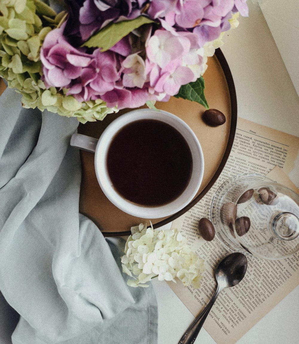 weiße Keramiktasse auf weißer Keramikuntertasse neben silbernem Löffel