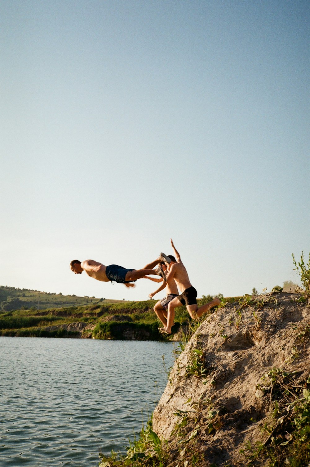 man in black shorts jumping on brown rock near body of water during daytime