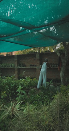 A gardener wearing protective clothing using gardening tools in a lush garden.