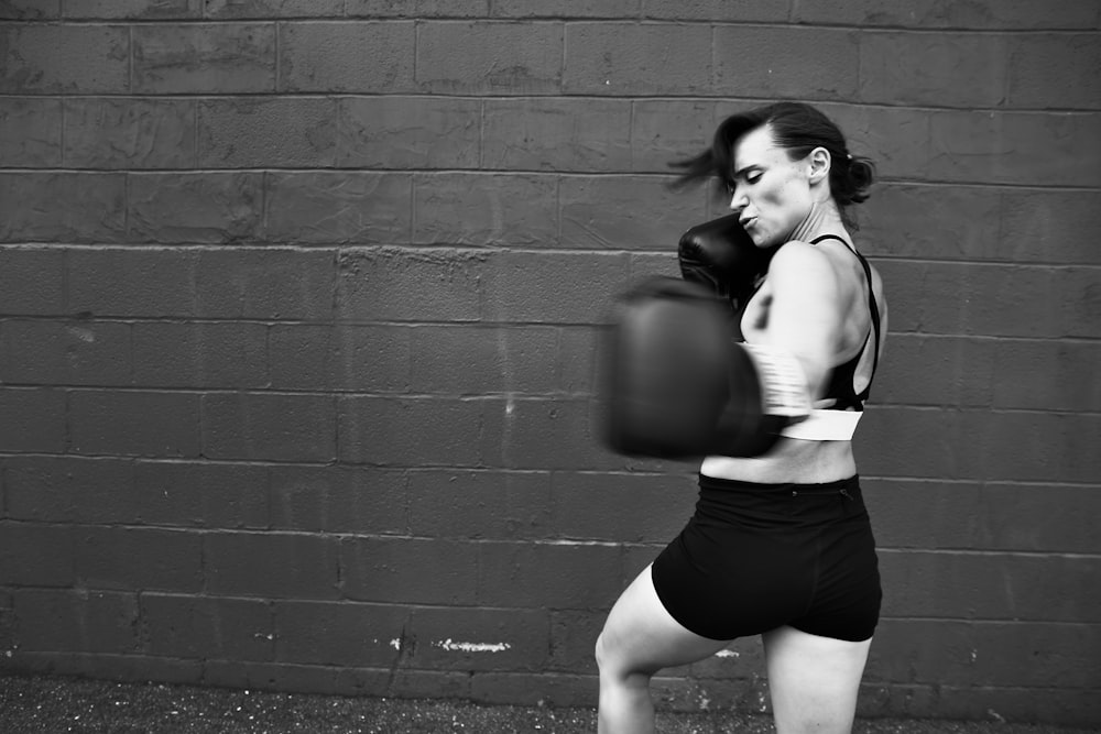 woman in white tank top and black shorts leaning on wall