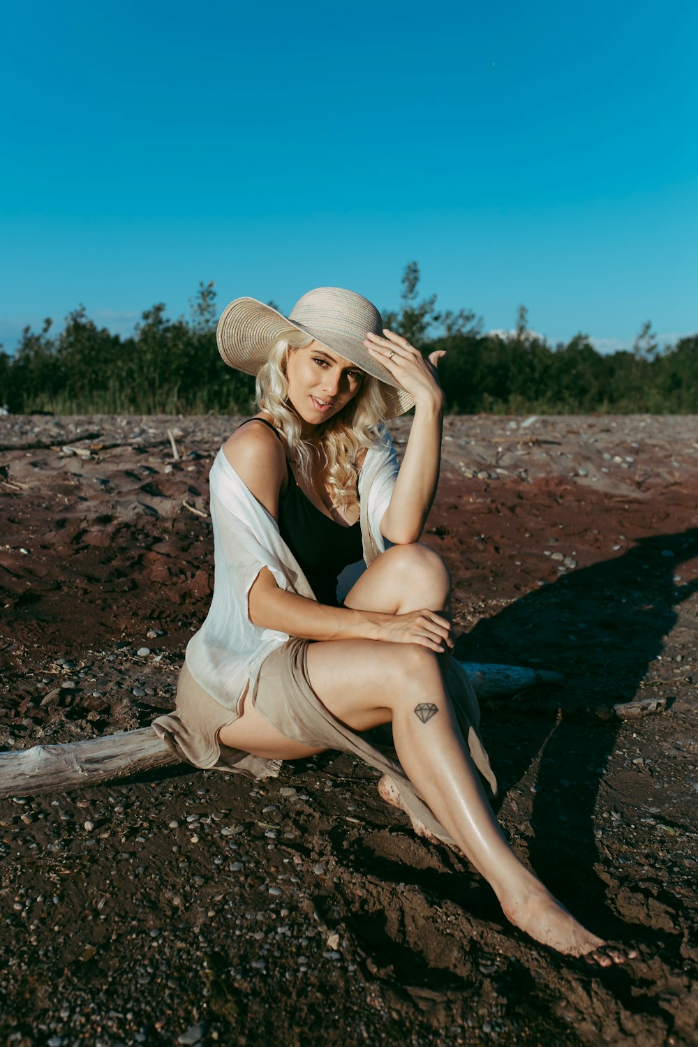 woman in white tank top and blue denim jeans sitting on brown wooden log during daytime