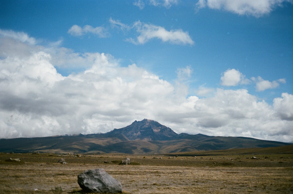 campo di erba marrone vicino alla montagna sotto il cielo blu durante il giorno