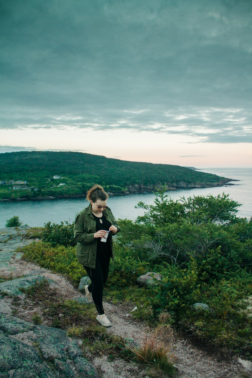 woman in green jacket standing on green grass field near body of water during daytime