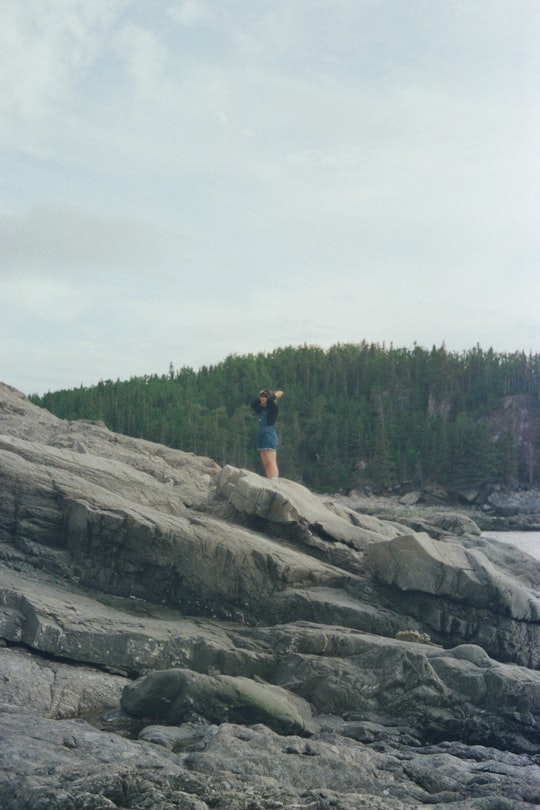 person in blue shirt and brown shorts standing on brown rock formation during daytime in Le Bic Canada