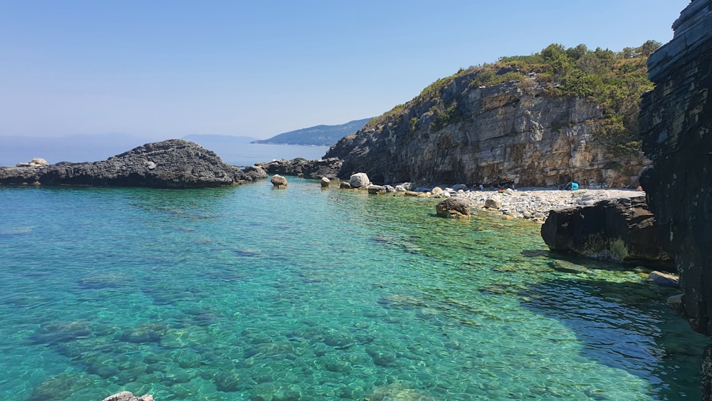 people swimming on sea near mountain during daytime