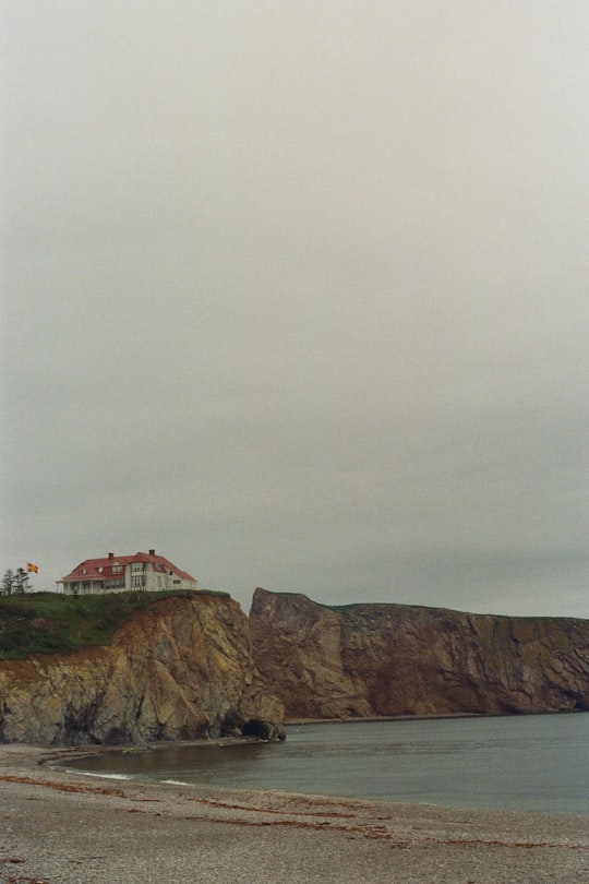 white and brown house on brown rock formation under white sky during daytime in Percé Rock Canada