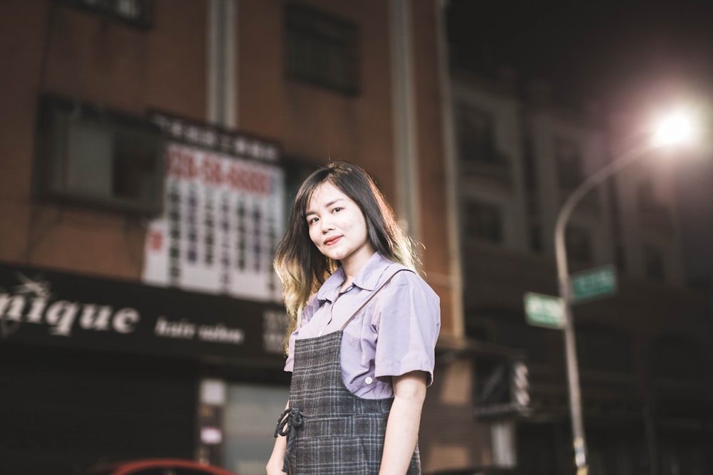 woman in blue button up shirt and black and white plaid skirt standing on street during