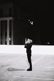 A shadowy figure observing a city street through binoculars at dusk.