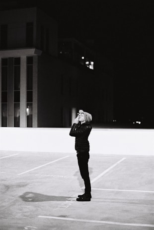 Investigator using binoculars to watch a suspect from a parked car at dusk.