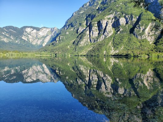 Green and gray mountain beside lake under blue sky during daytime