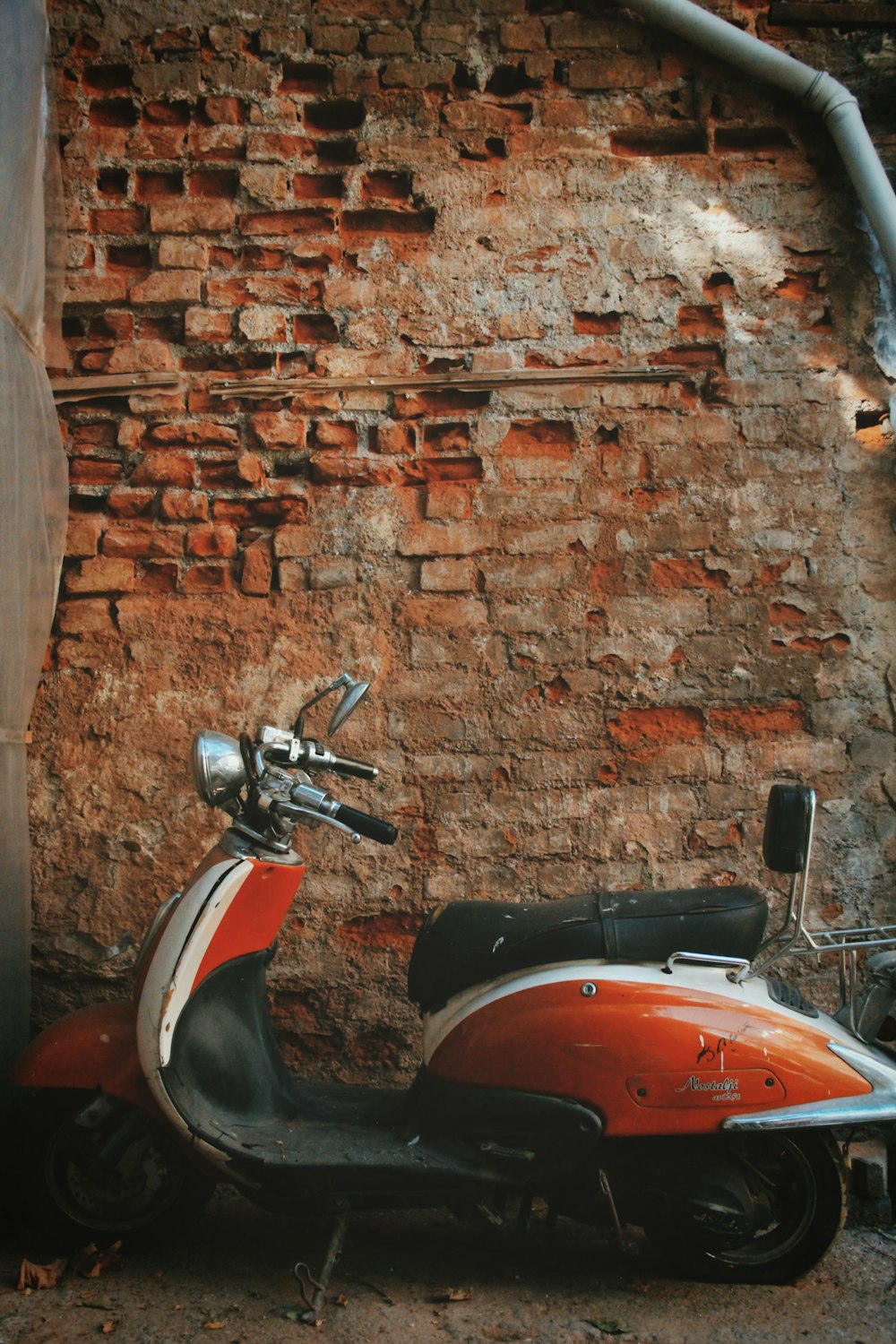 red and black motor scooter parked beside brown brick wall