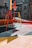 A colorful urban playground with a basketball hoop attached to a multicolored backboard. The ground is painted with geometric patterns, and there is a swing set nearby. The setting is surrounded by buildings, giving it a vibrant, urban feel.