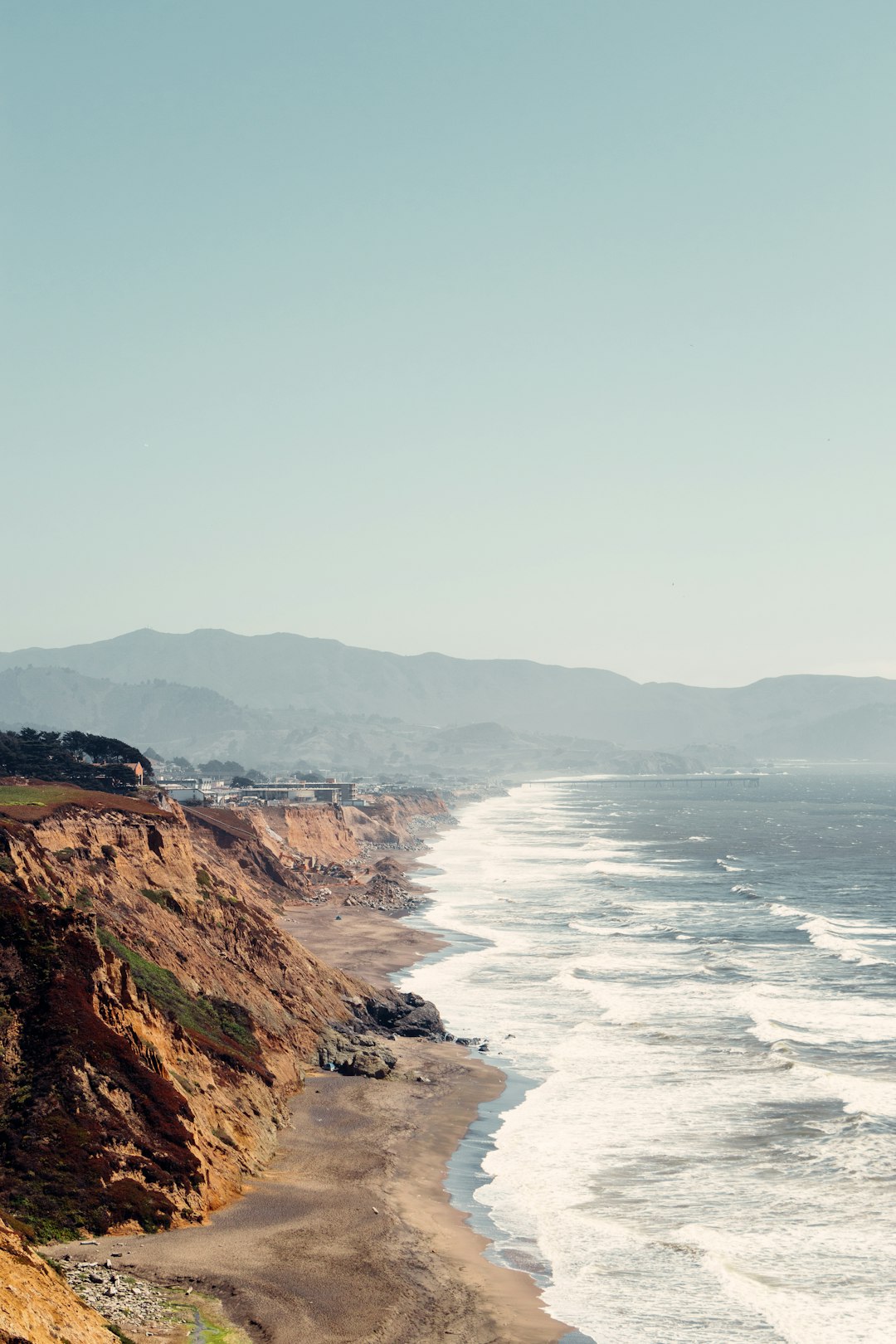 brown rocky mountain beside sea during daytime