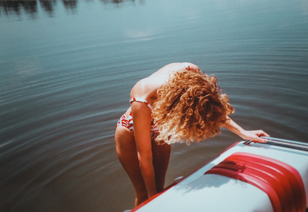 woman in blue bikini lying on red and white surfboard