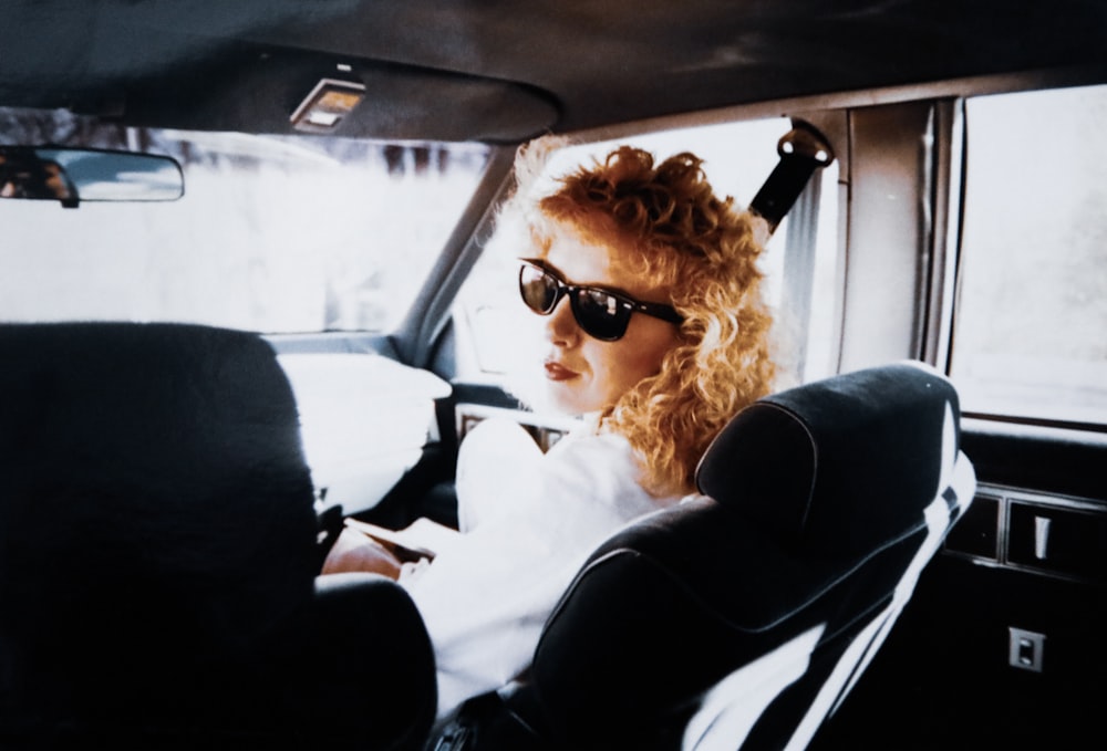 woman in white shirt wearing black sunglasses sitting on car seat