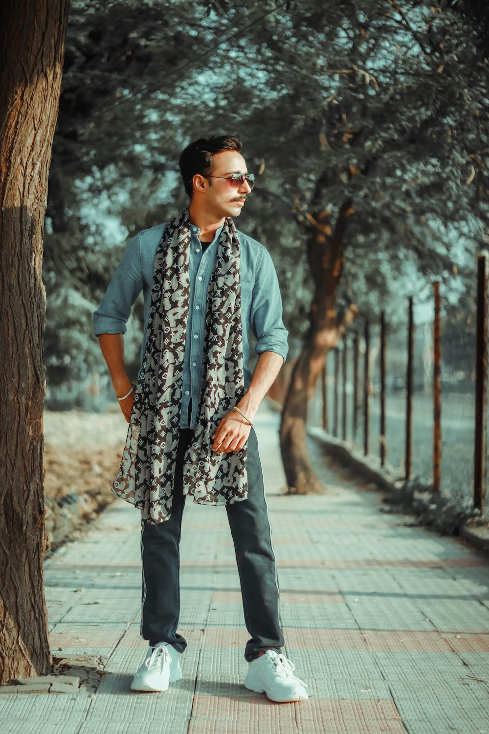 man in blue denim button up shirt and black and white floral pants standing on sidewalk