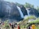 A vibrant photo of travelers enjoying a lush waterfall in Mauritius under bright sunlight.