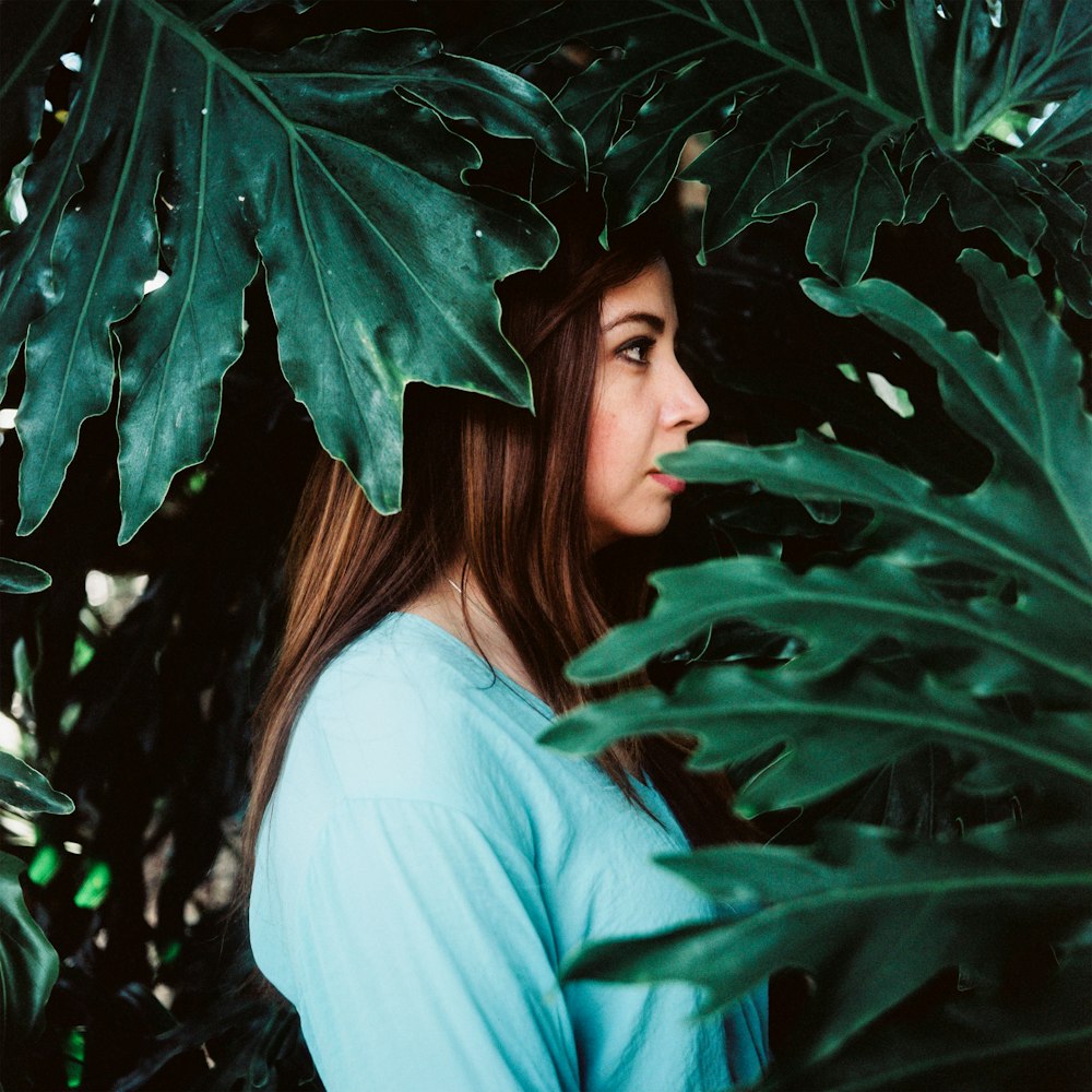 woman in white long sleeve shirt standing beside green leaves