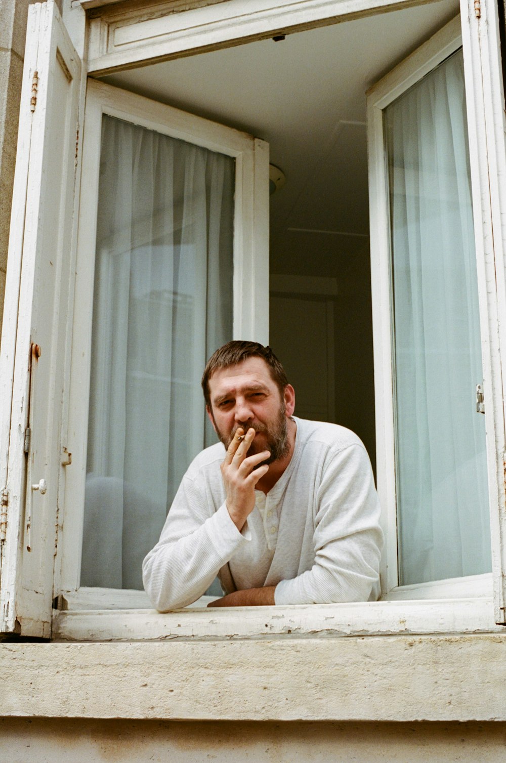 man in white dress shirt sitting beside white wooden framed glass window