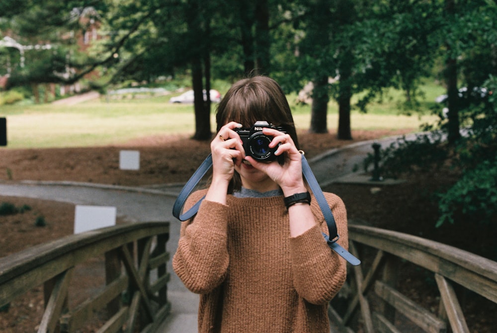 woman in brown knit sweater holding black dslr camera