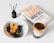 A book titled 'Lean Analytics' lies on a table next to a glass of coffee. There is a brown bottle labeled 'Rosemary' with diffuser sticks and a white bowl containing a dessert topped with caramel and accompanied by olives.