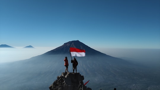 person standing on rock near mountain under blue sky during daytime in Temanggung Indonesia
