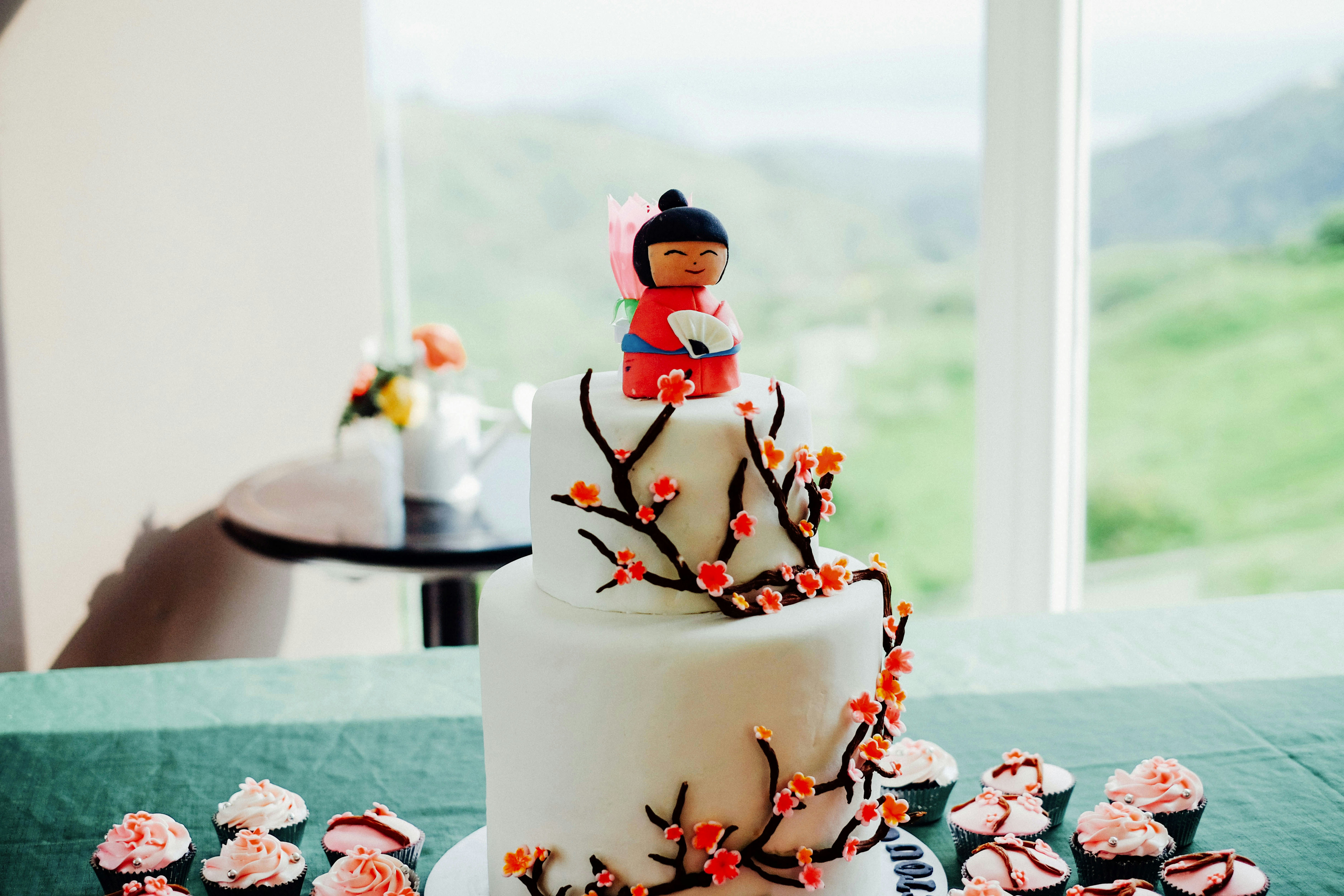 A white fondant cake with a girl in a kimono as a cake topper, surrounded by pink frosted cupcakes